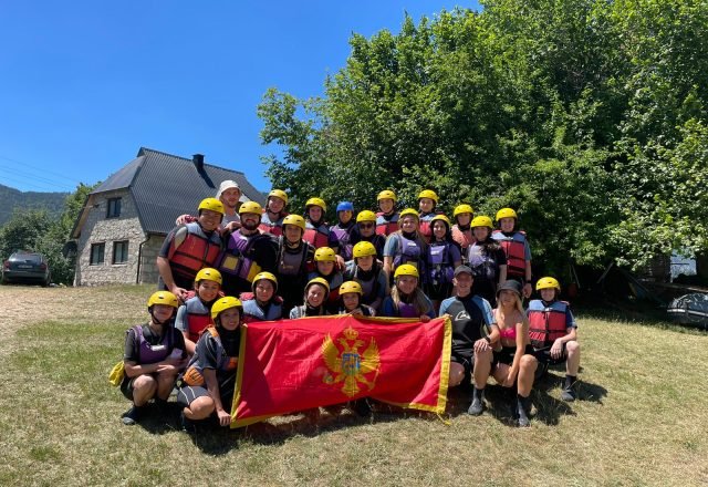 A group in helmets and life jackets holding a Montenegro flag